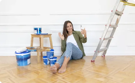 A smiling woman taking a relaxing break with a drink while painting a room in her home.