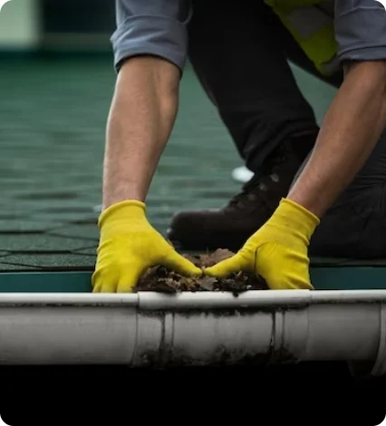 A worker wearing yellow gloves cleaning leaves and debris.