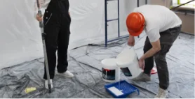 Two painters preparing cans of paint and rollers before starting an interior project.